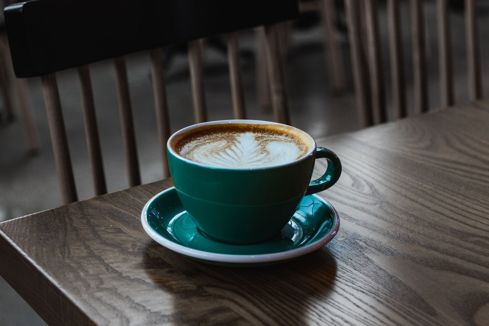 Latte with leaf art in a green cup on a wooden café table