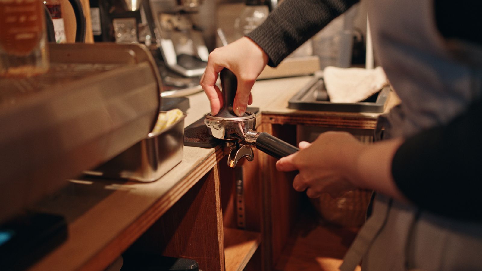 Barista tamping coffee grounds beside an espresso machine