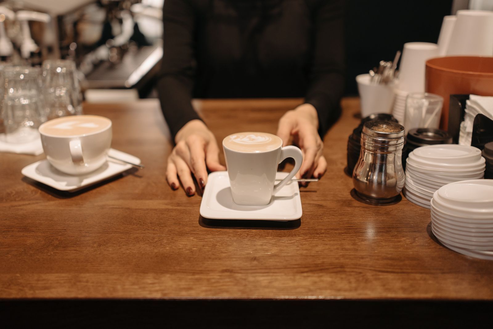 Barista serving two cappuccinos with latte art on a wooden counter